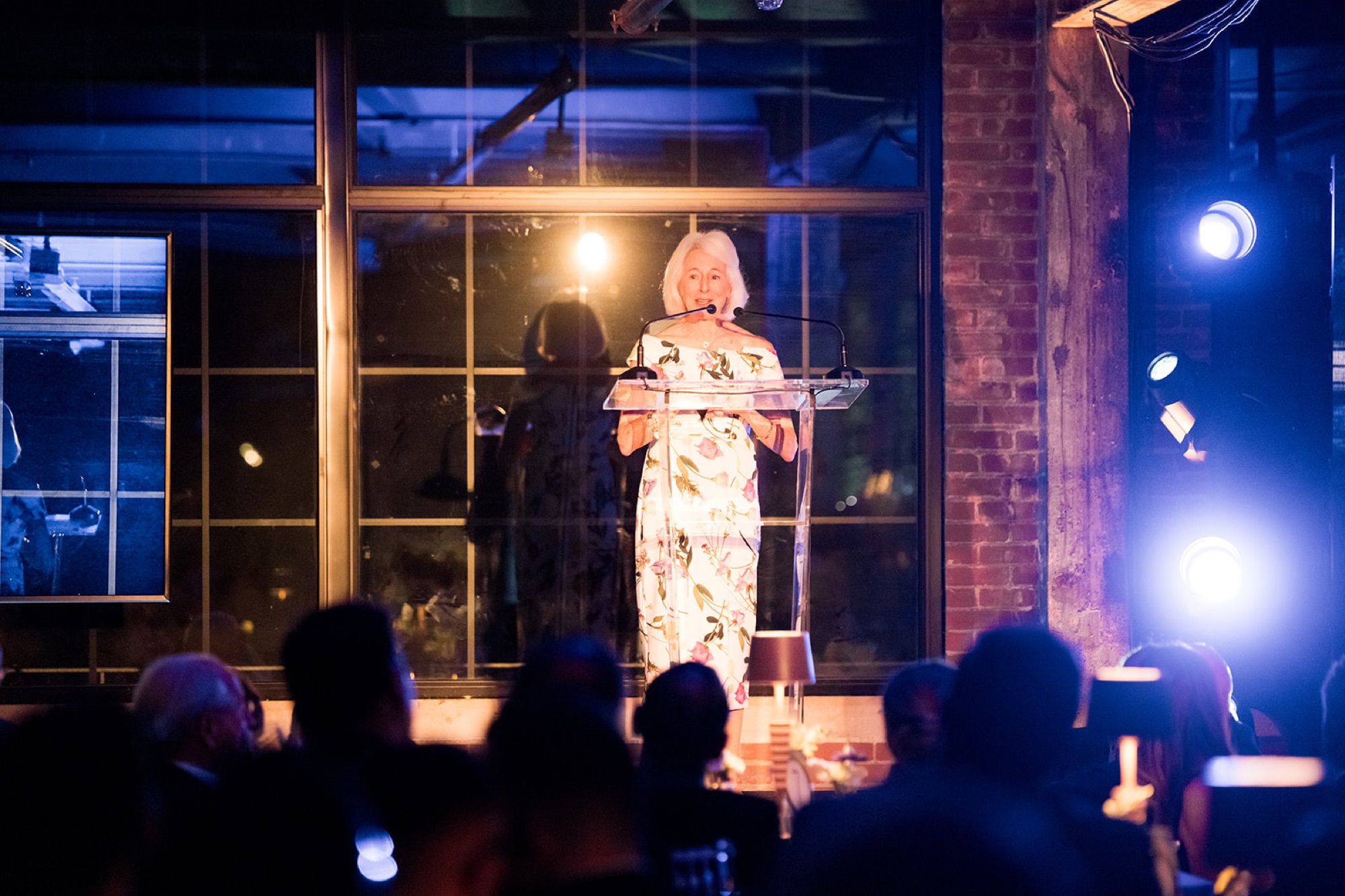 A speaker at the podium under the steel windows